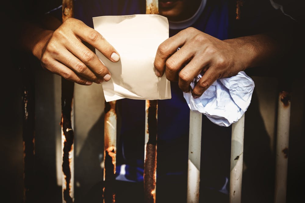 دستان یک مرد پشت میله‌های زندان کاغذ نامه را در دست گرفته است. عکس از شاتراستاک
