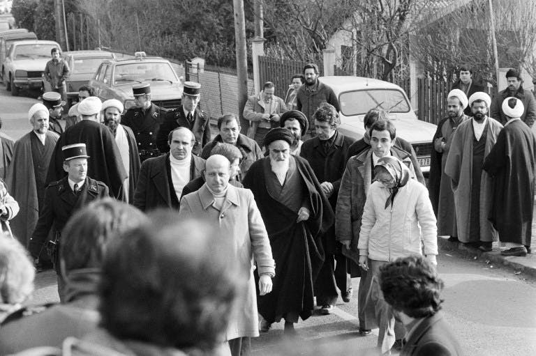 خمینی برای بازگشت به ایران نوفل لوشاتو را به سوی فرودگاه ترک می‌کند؛ دومین شخص در عقب تصویر با عمامه و عینک، حسن روحانی، رئیس‌جمهوری کنونی در میان دیگر همراهان است ــ عکس: AFP