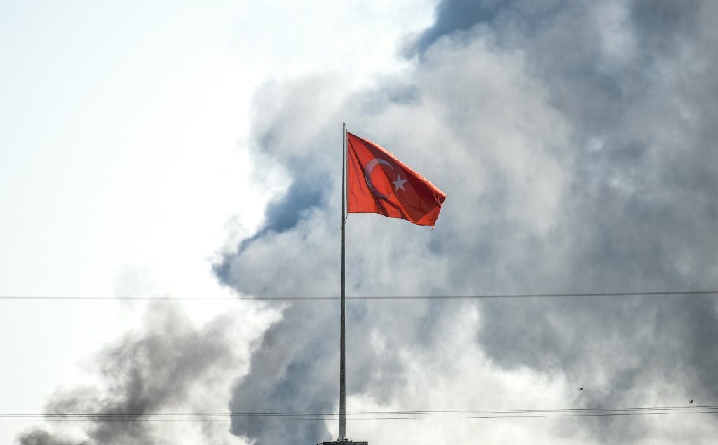 A picture taken in Akcakale at the Turkish border with Syria on October 10, 2019 shows the Turkish flag as smokes rises from the Syrian town of Tal Abyad after a mortar landed in Akcakale. - At least 18 people were injured in shelling on a Turkish border town on October 10, local media said, a day after Turkey launched an operation against Kurdish forces in northern Syria. (Photo by BULENT KILIC / AFP)