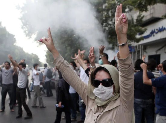 زنی معترضی به دوربین علامت پیروزی نشان می‌دهد