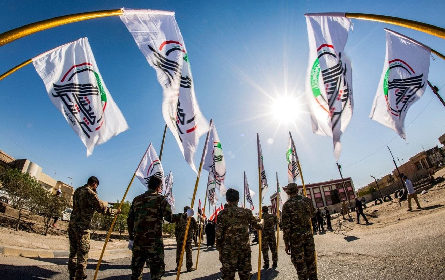 پرچم‌های گروه‌های شبه‌نظامی وابسته به سپاه قدس در عراق بر فراز سر چند نفر از اعضای این گروه‌ها