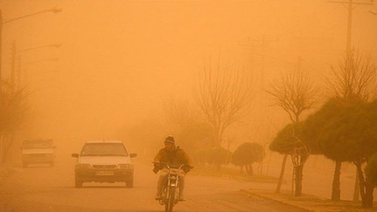 تصویری از آلودگی هوای خوزستان که در آن هوا نارنجی شده است. در تصویر یک موتور سیکلت، و دو خودرو در حال حرکتند.