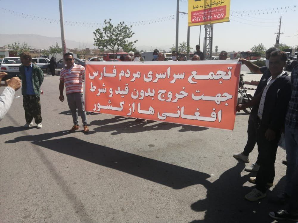 دو مرد یک پلاکارد که بر روی آن نوشته شده است «تجمع سراسری مردم فارس جهت خروج بدون قید و شرط افغانی‌ها از کشور» را در دست دارند.