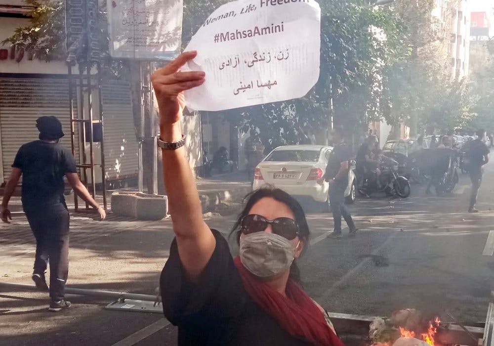 زنی در خیایان در میانه اعتراضات نوشته ای در دست دارد با شعار زن زندگی و آزادی