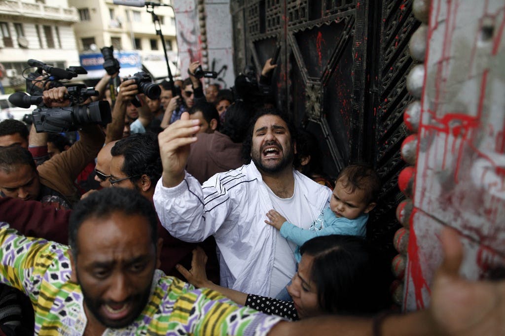 تصویر در مقابل دادگاهی در مصر در سال ۲۰۱۳ که علا عبدالفتاح فعال دموکراسی خواه مصری با فرزند کوچکش در بغل دیده می‌شود