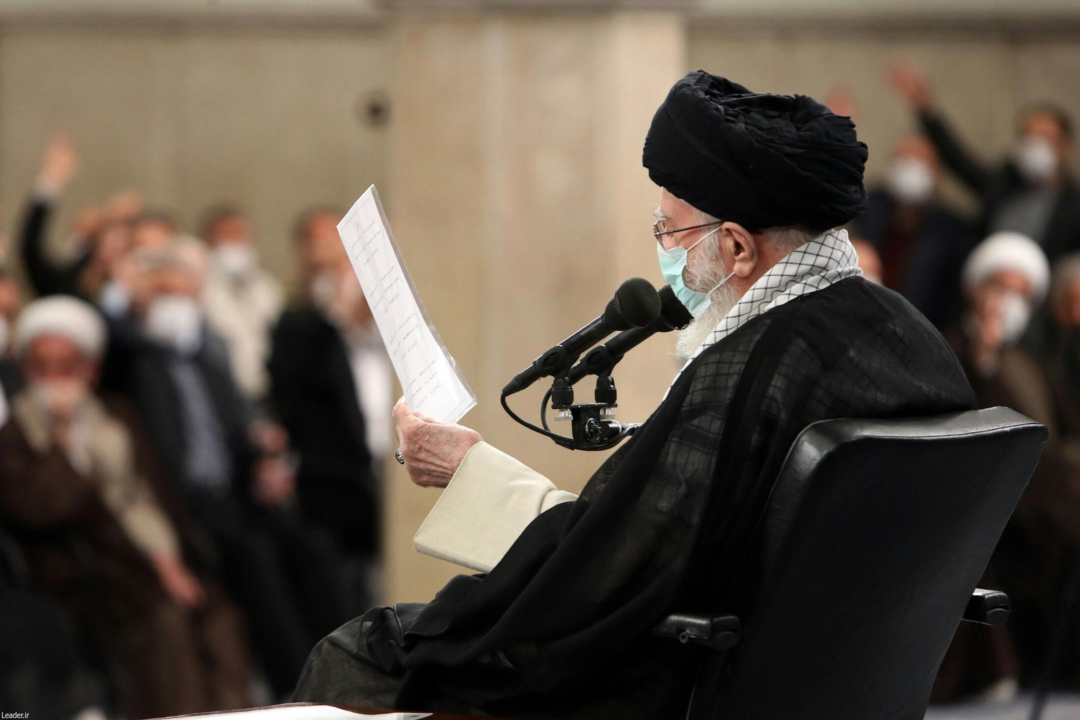 عکسی از زاویه پشت سر خامنه‌ای در حالی که کاغذی در دست دارد و به آن نگاه می‌کند