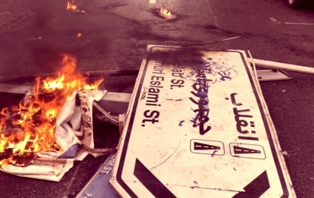 تصویر تابلو خیابان‌های انقلاب و جمهوری اسلامی روی زمین و در کنار آتش که به شکل نمادین روی جمهوری اسلامی خط کشیده است.ر