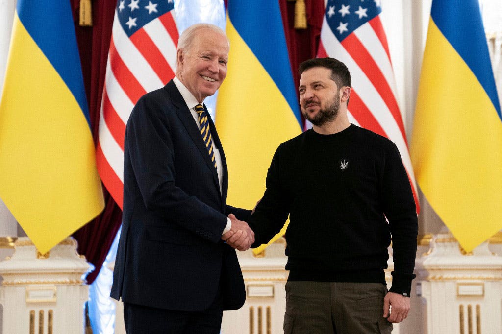 جو بایدن، رئیس‌ جمهوری آمریکا در زیر پرچم‌های ایالات متحده و اوکراین با ولودیمیر زلنسکی دست داده است. هر دو می‌خندند. دیدار آن‌ها با سفر بایدن به کی‌یف در تاریخ ۲۰ فوریه ۲۰۲۳ / یکم اسفند ۱۴۰۱ ممکن شد.