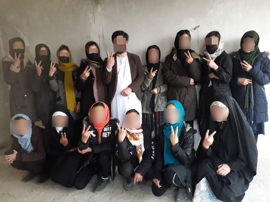 معلم مرد و شاگردان دخترش در یک کلاس زیر زمینی آموزش به دختران در نقطه‌ای از افغانستان تحت حکومت طالبان نشان پیروزی نشان می‌دهند