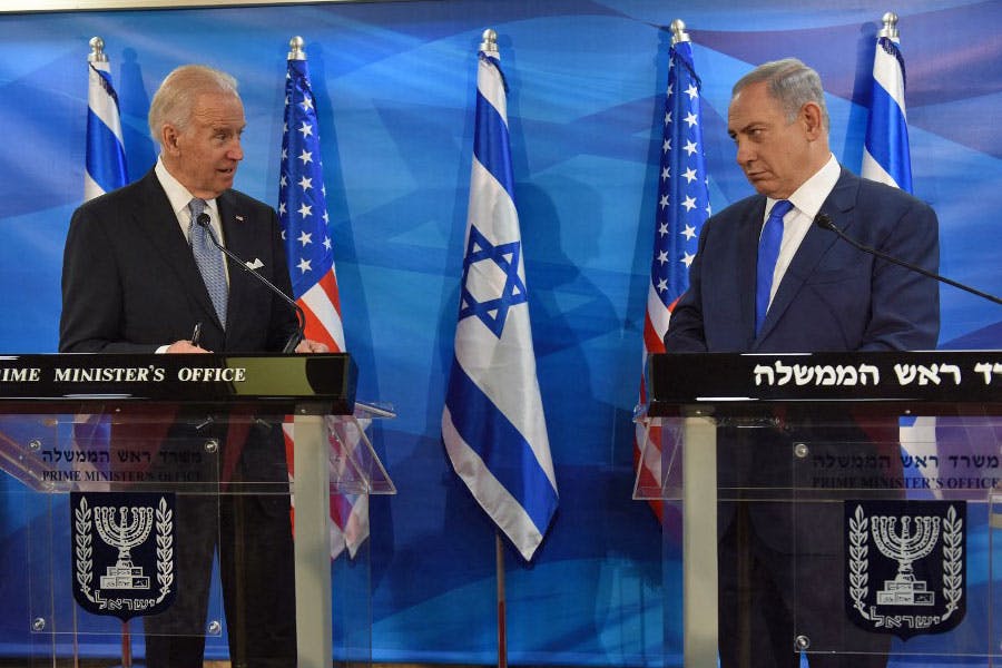 بنیامین نتانیاهو، نخست‌وزیر اسرائیل در طرف راست تصویر به جو بایدن، رئیس جمهوری آمریکا بدون لبخندی بر لب نگاه می‌کند و بایدن با نگاهی جدی در حال حرف زدن است. در پشت آن‌ها پرچم‌های اسرائیل و آمریکا دیده می‌شود.