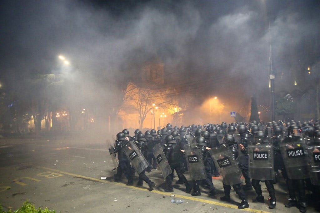 در تصویر ده‌ها پلیس ضد شورش گرجستان را می‌بینیم که در میان دود و آتش با سپرهایی در دست و کلاه‌خودها بر سر، در خیابانی در تفلیس، پایتخت گرجستان به سمت تظاهرکنندگان معترض در حرکت هستند.