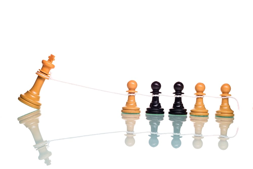 چند مهره سرباز شطرنج از هر دو رنگ سیاه و سفید با یک طناب مهره شاه سفید را سرنگون می‌کنند.