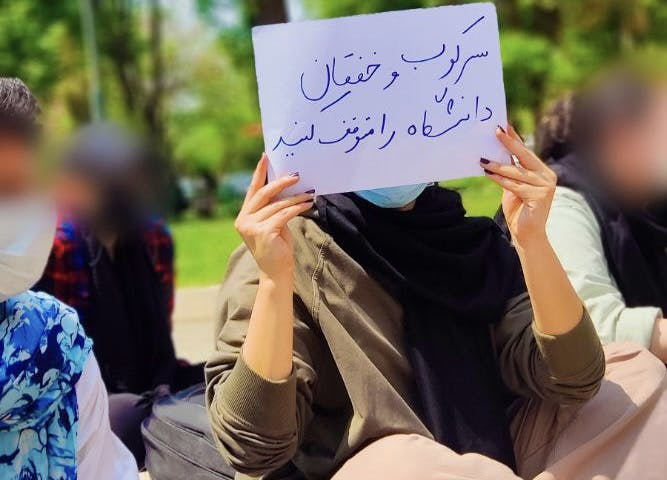 تصویر یک دانشجوی دانشکده روانشناسی دانشگاه تهران با پلاکاردی در دست با این متن که سرکوب و خفقان دانشگاه را متوقف کنید