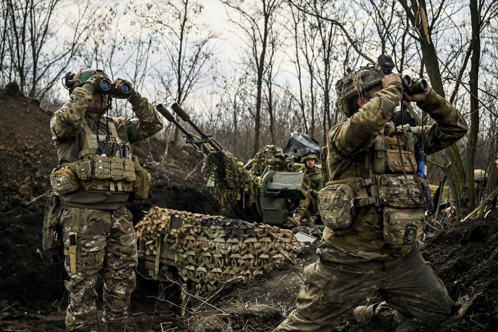 دو سرباز اوکراینی با دوربین‌های خود دوردست را زیر نظر دارند. پشت سر آن‌ها یک سرباز دیگر در کنار عراده توپ نشسته است.