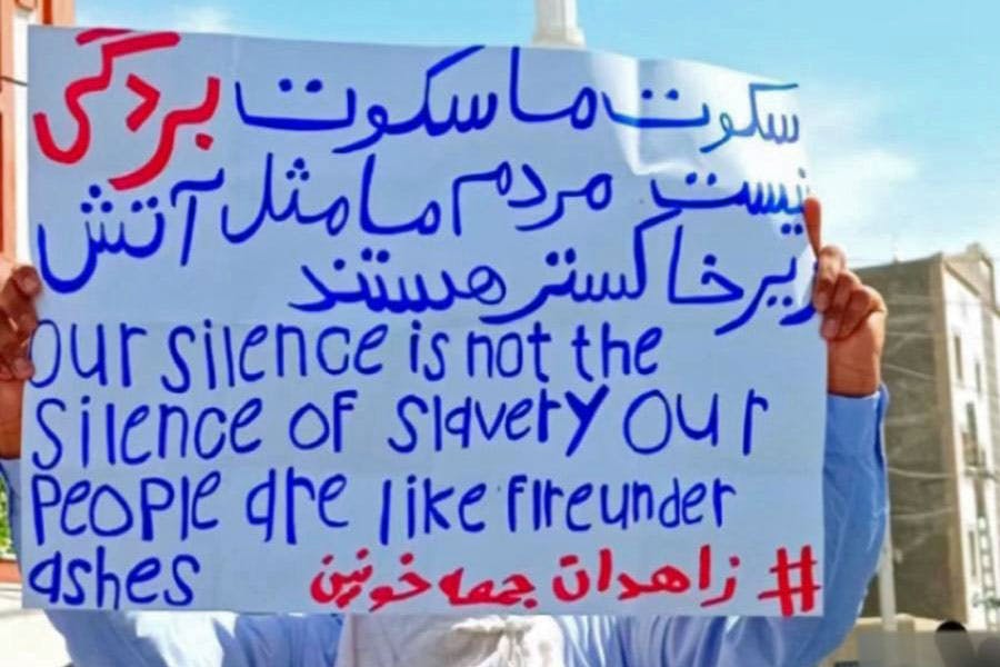 یک کاغد که بر آن نوشته شده است سکوت ما سکوت بردگی نیستن. مردم ما مثل آتش زیرخاکستر هستند. در دست یکی از معترضان بلوچ