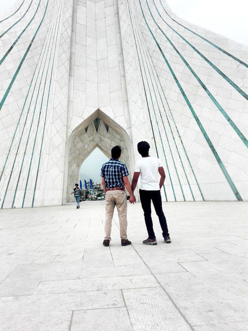 دو نفر دست در دست همدیگر روبروی برج آزادی در تهران