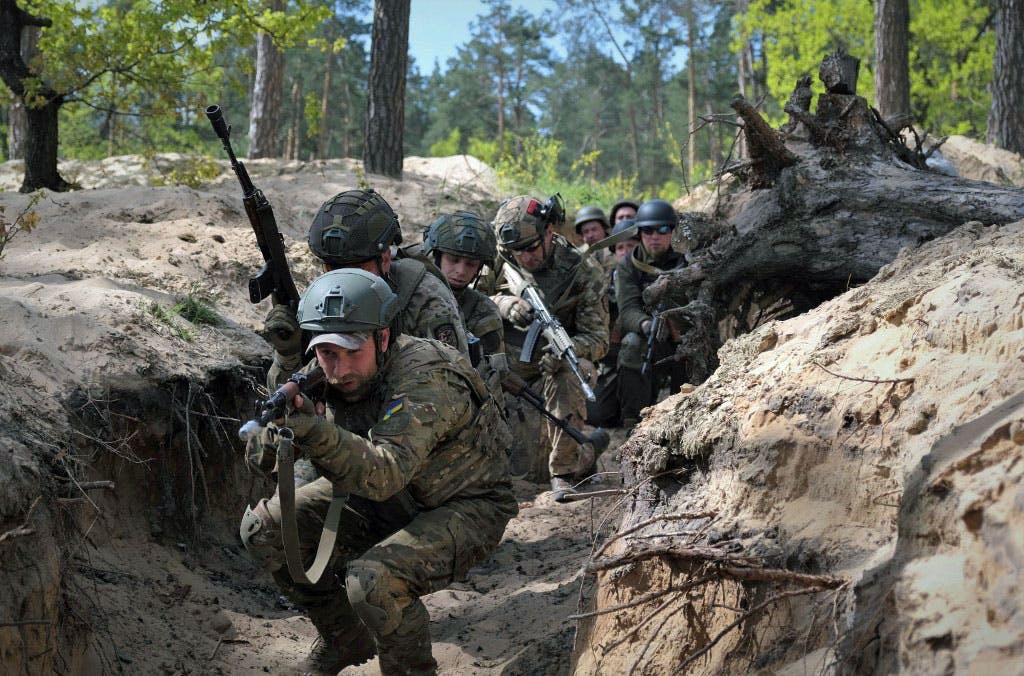 در تصویر چند سرباز اوکراینی دیده می‌شوند که در شیار سنگری در یک جنگل با سلاح‌هایی در دست پشت سر هم در حال پیشروی هستند.