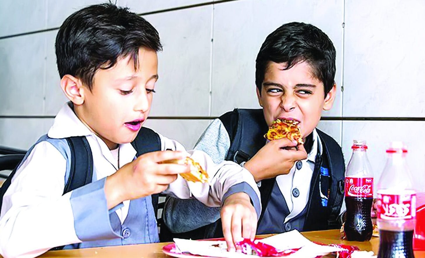 دو کودک در حال خوردن پیتزا و نوشابه کوکاکولا