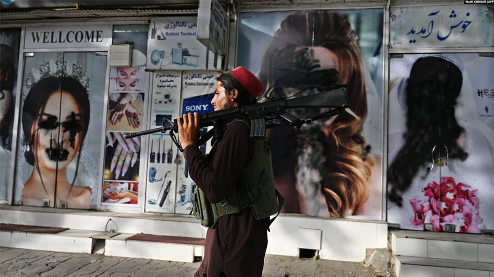 یک سرباز مسلح طالبان در پس‌زمینه پوسترهایی از تصویر زنان که روی آنها رنگ ریخته شده است