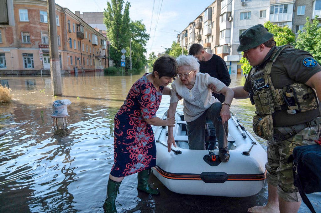 در حالی‌که همه جا را آب فراگرفته، سربازان اوکراینی و یک زن در حال کمک به پیاده شدن یک زن سالمند از قایق هستند.