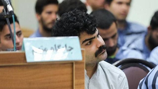 تصویری از سامان یاسین در دادگاه. او می‌گوید به دستور قاضی صلواتی ریش او را زده‌اند و او را با سبیل به جلوی دوربین‌های مستقر در دادگاه برده‌اند.