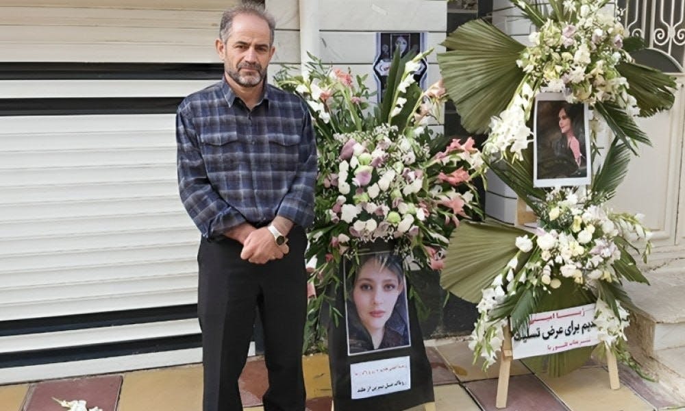 تصویر امجد امینی، پدر ژینا (مهسا) امینی در کنار عکس‌های دخترش. به او و خانواده‌اش اجازه برگزاری مراسم سالگرد و حضور بر سر خاک دخترشان داده نشد.