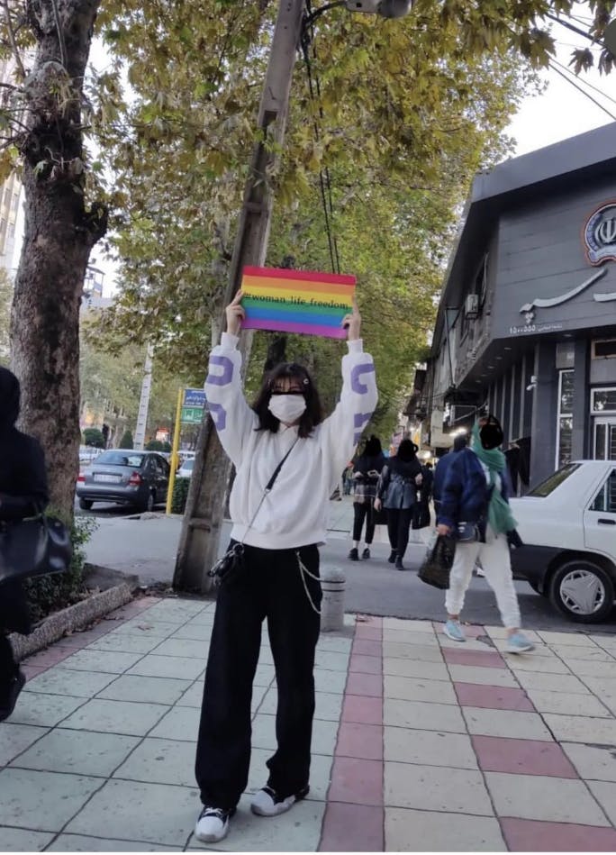 تصویری از یک فرد معترض با پرچم رنگین‌کمانی در یک خیابان ایران در گذر جنبش زن، زندگی، آزادی