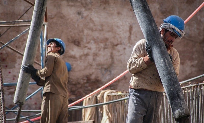 دو کارگر در یک پروژه احتملا نفت و گاز با لباس کار و در حالی بلند کردن دو لوله فلزی بلند.