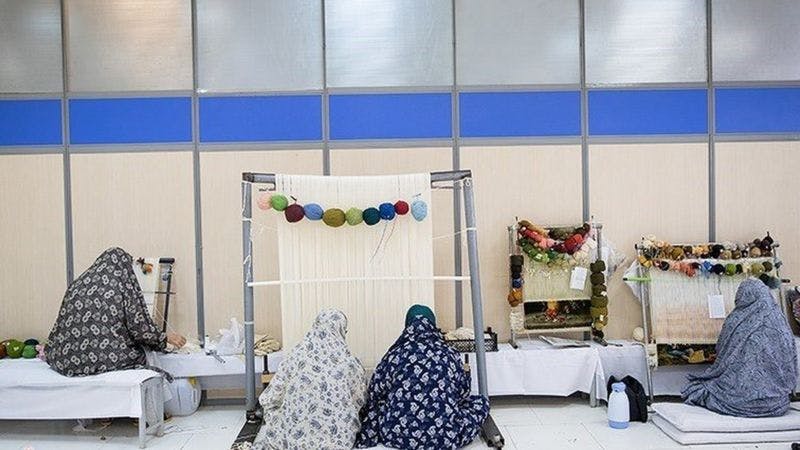 چهار زن چادرپوش از نمای پشت سر در حال بافتن قالی در زندان هستند