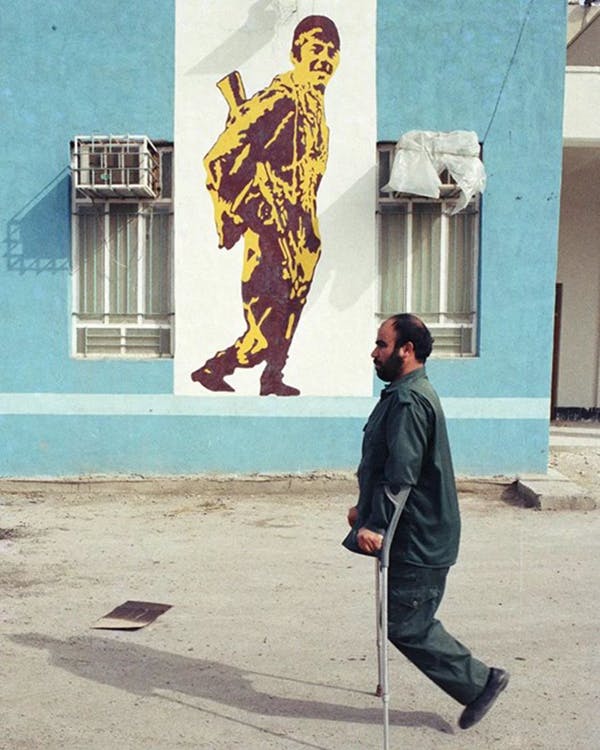 از قربانیان جنگ ایران و عراق. از جبهه برگشته. دیوارنگاره تشویق می‌کند که به جبهه بروید− عکس از مهدی منعم