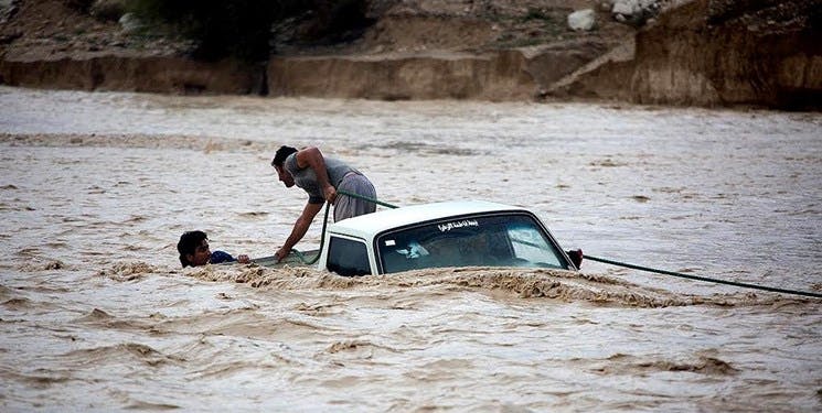 نمای یک ماشین غرق شده در سیلاب و دو فرد