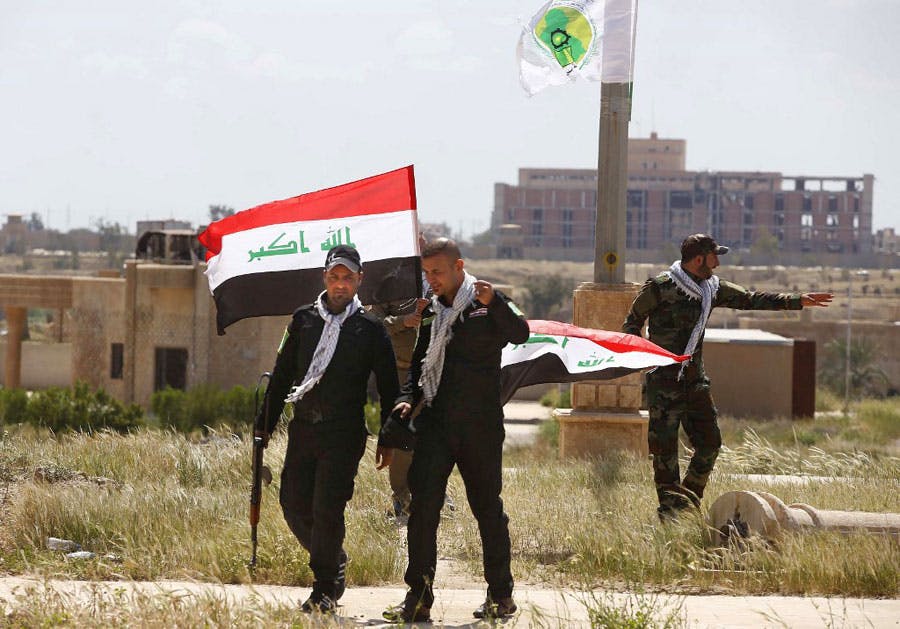 در تصویر سه نفر از شبه‌نظامیان حشد الشعبی عراق در کنار پرچم این کشور دیده می‌شوند.