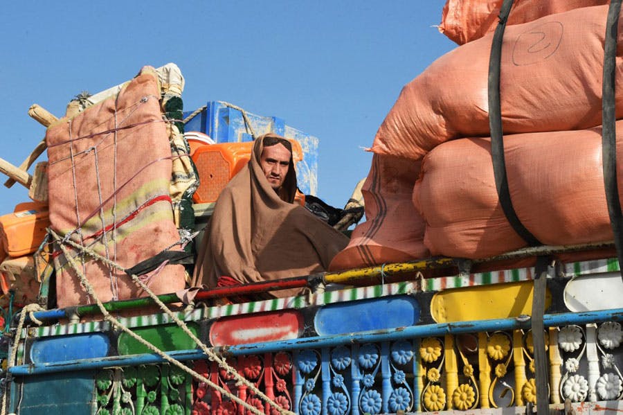 در تصویر یک مرد پناهجوی افغان دیده می‌شود که در میان وسایل خود سوار بر کامیونی در حال عبور از مرز پاکستان و افغانستان است.