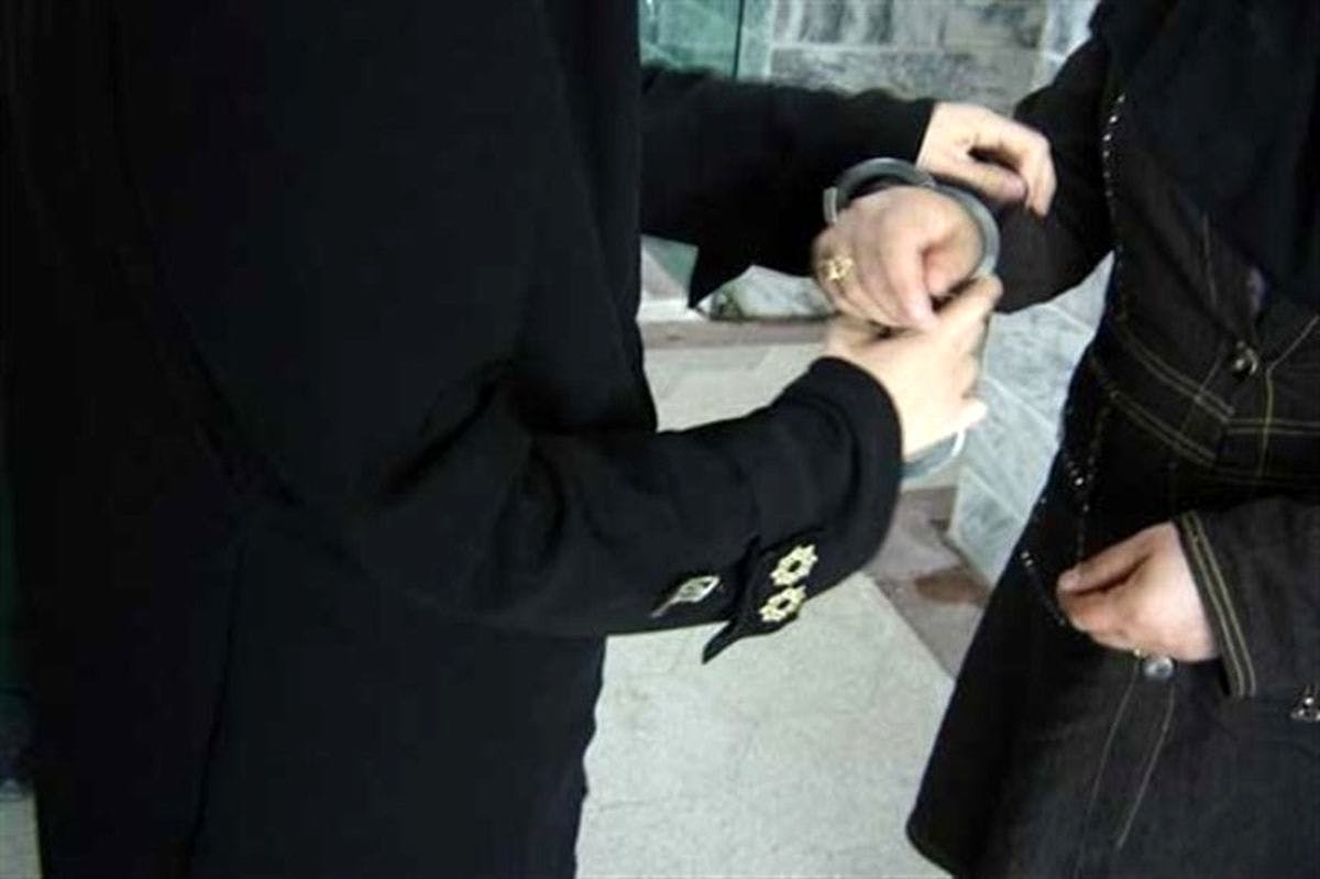 یک مأمور به‌ دستان زنی دستبند می‌زند