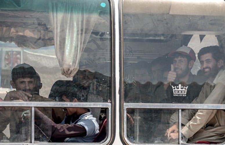 صورت چند افغانستانی از پشت شیشه‌های اتوبوسی فرسوده در مهمانشهر تربت جام دیده می‌شود.