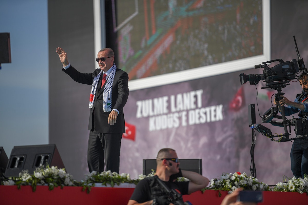 اردوغان روی یک سن ایستاده و خطاب به حاضران لبخند می‌زند و دست تکان می‌دهد