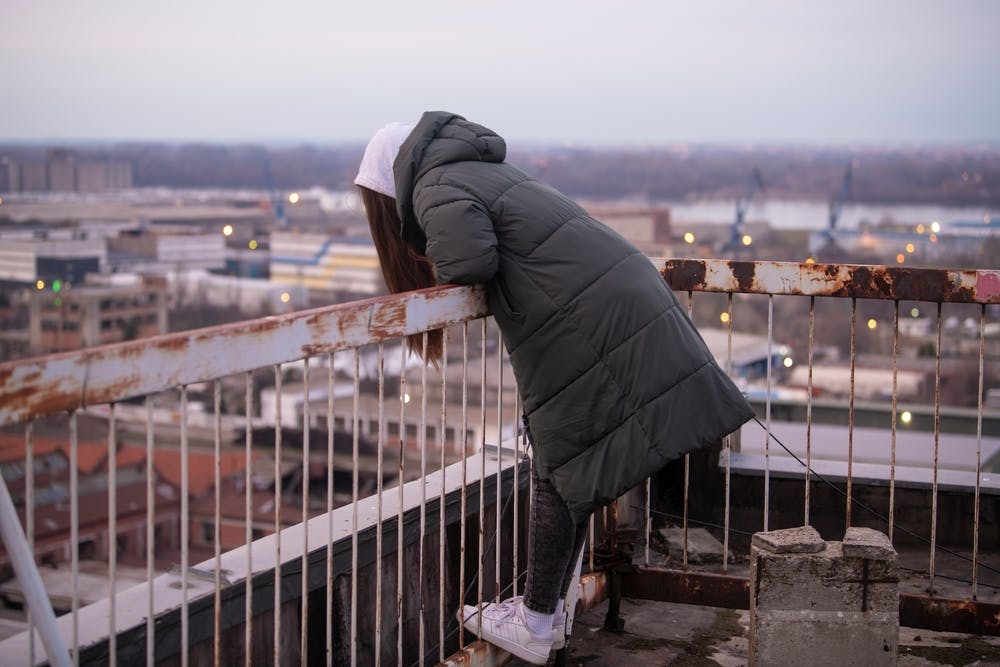زنی در پشت بام ساختمانی بر روی نرده خم شده و گویی به خودکشی فکر می‌کند