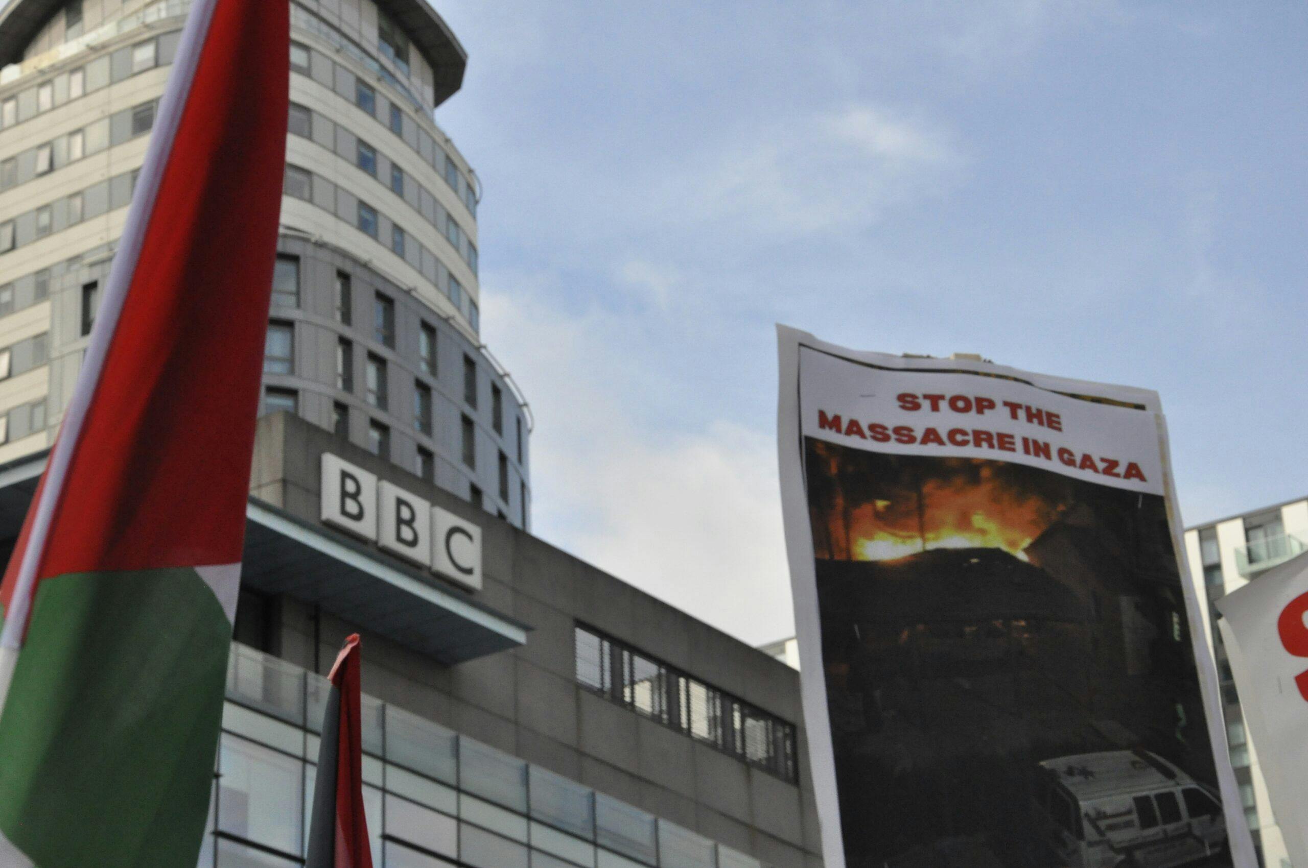 معترضی پوستری را جلوی دفتر بی‌بی‌سی بالا گرفته است که روی آن نوشته شده به قتل‌عام در غزه پایان دهید