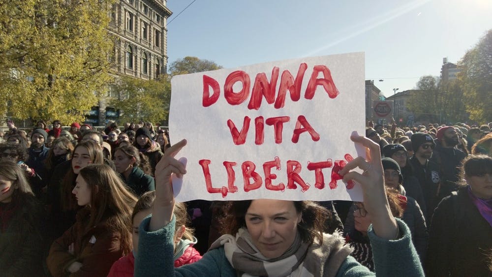 ایتالیا، میلان ۲۵ نوامبر ۲۰۲۳، روز جهانی منع خشونت علیه زنان، تظاهرات زنان معترض پس از مرگ جولیا جکتین، یک زن شعار زن‌، زندگی، آزادی به ایتالیایی را روی کاغذ بالای سر برده است.