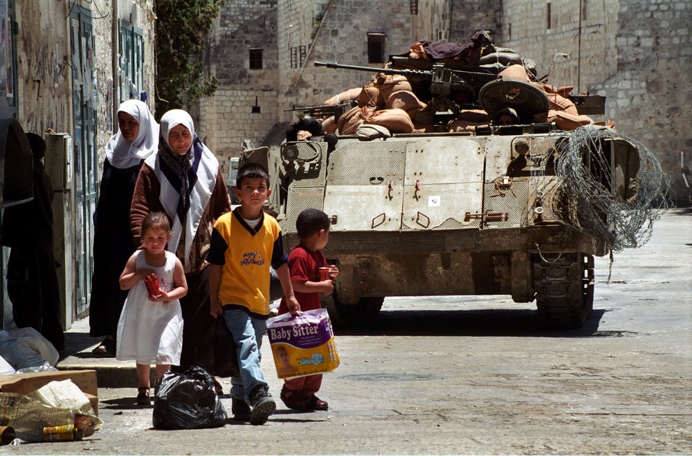 ساکنان فلسطینی بیت لحم - دو زن با کودکانشان جلوی یک تانک اسرائیلی که حین منع آمدوشد در نزدیکی میدان منگر مستقر شده دیده می‌شوند. تاریخ عکس ۲۸ مه ۲۰۰۲ - عکس از شاتراستاک