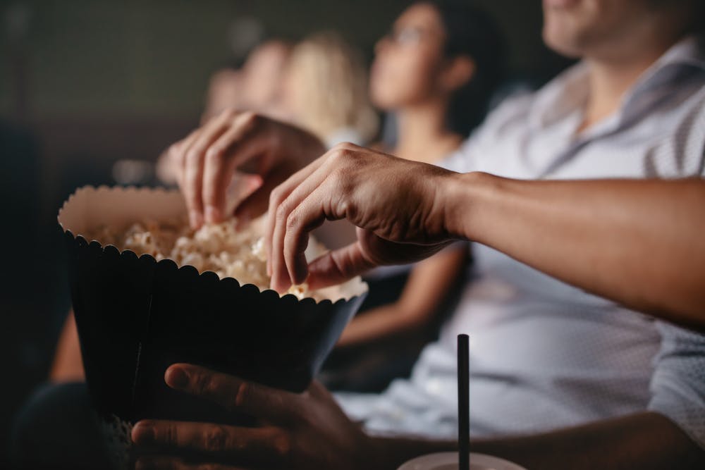 تصویری از چند تماشاگر در یک سالن سینما در حال خوردن پاپ‌کورن - عکس از شاتراستاک