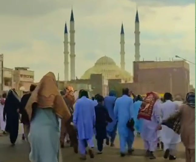 دوربین از پشت جمعی از مردم بلوچ را در حال راهپیمایی نشان میدهد. در افق دوردست مسجد مکی پیداست