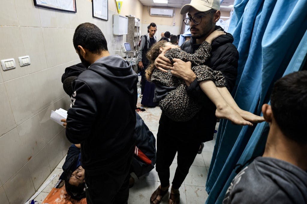 محتوای گرافیکی / تصویری از بیمارستان ناصر در خان یونس در جنوب نوار غزه، پس از حملات اسرائیل در ۳ دسامبر ۲۰۲۳:‌ مردی دختری مجروح را حمل می‌کند. یک زخمی دیگر روی زمین خوابیده است. (عکس از محمود حمس / خبرگزاری فرانسه)