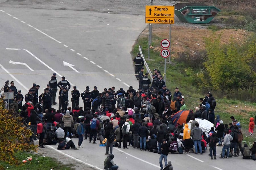 جمعیتی از پناهجویان در وسط جاده‌ای دیده می‌شوند و مأموران مرزی کرواسی آن‌ها را احاطه کرده‌اند.