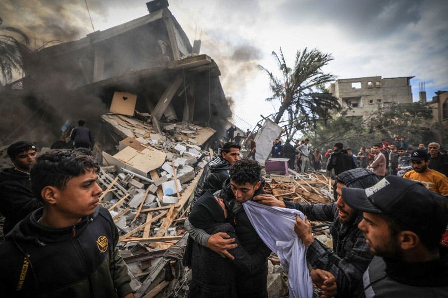 در میان دود و ویرانه‌های یک ساختمان پس از بمباران اسرائیل در رفح، زنی پسر نوجوانی را در آغوش گرفته و گریه می‌کند. جوان‌های دیگر ناراحت در اطراف آن‌ها ایستاده‌اند.