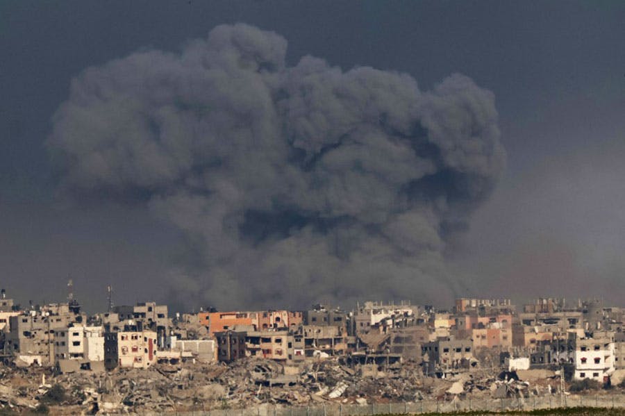 در تصویر دود عظیم و سیاه بمباران هوایی اسرائیل بر آسمان غزه دیده می‌شود. ساختمان‌های ویران در پایین تصویر مشخص هستند.