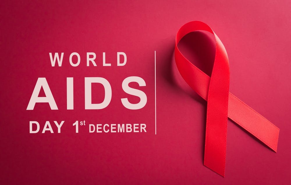 پس‌زمینه قرمز رنگ، با یک روبان قرمز در سمت راست. در سمت چپ به انگلیسی نوشته: روز جهانی ایدز، یکم دسامبر