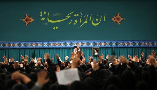 شعار «زن ریحانه است» در ابعاد خیلی بزرگ بالای سر خامنه‌ای نقش بسته و برای جمعیت زنان روبه‌رویش دست تکان می‌دهد