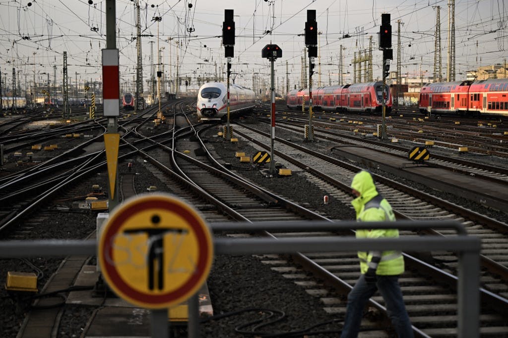 ایستگاه قطار در فرانکفورت آلمان ۱۰ ژانویه ۲۰۲۴ دومین روز اعتصاب رانندگان قطار. دو قطار در فاصله دور توقف کرده‌ند و یک کارگر در حال عبور از میان ریل‌ها است. عکس AFP