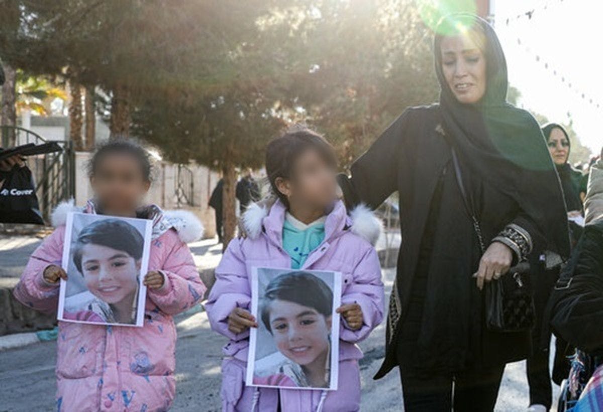 دو کودک همراه با مادرشان عکس یک کودک کشته شده در انفجارهای کرمان را در دست دارند.